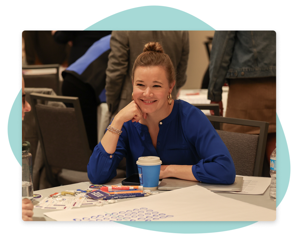 A teacher smiling while sitting at a table, in front of a paper with math exercises on it.