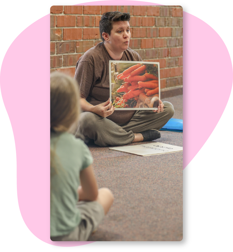 Group Reading Photo A teacher holding up a photo of carrots to their students while reading a story.