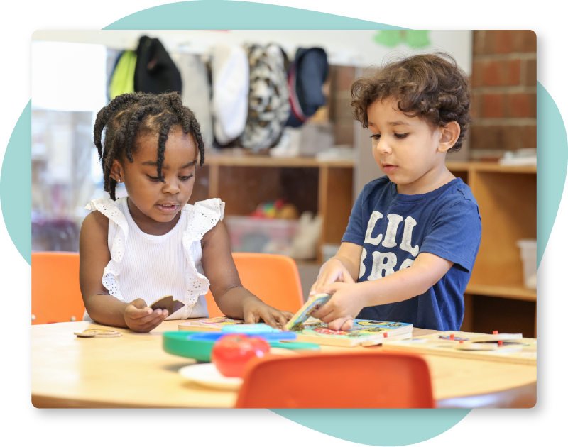 Two Students at Table Two young children working on a puzzle together.