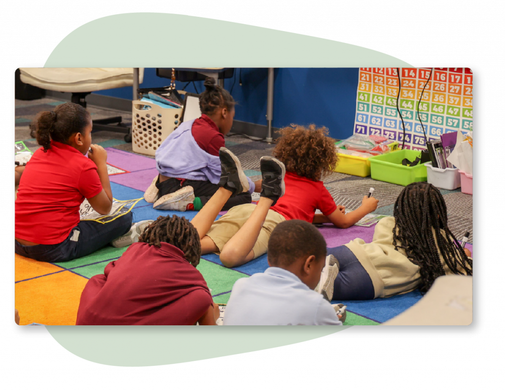 A group of first graders sitting on the floor of a classroom.